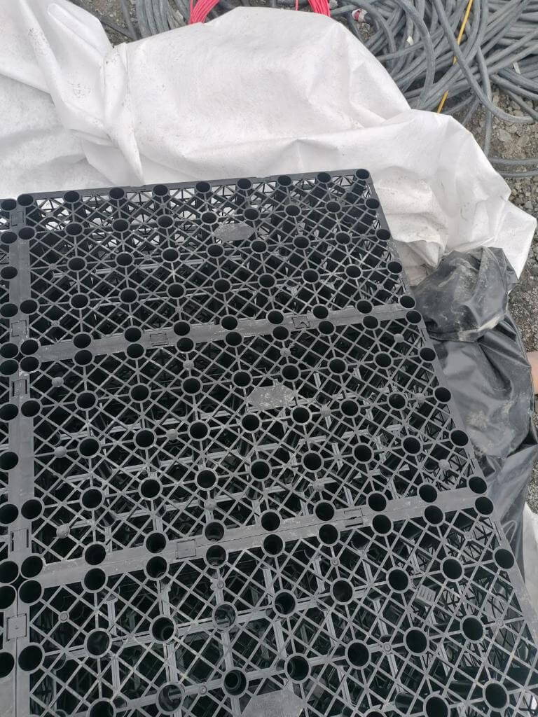 Black plastic grid with circular holes on white cloth and gray cables in the background